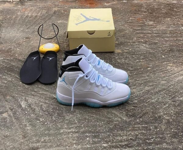 A pair of white and blue Air Jordan 11 sneakers with a yellow shoe box and black slippers on a concrete floor, perfect for sneaker enthusiasts in Nigeria.