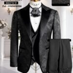 A mannequin wearing a black floral pattern suit with satin lapel, white shirt, and black bow tie, with matching trousers displayed beside it.