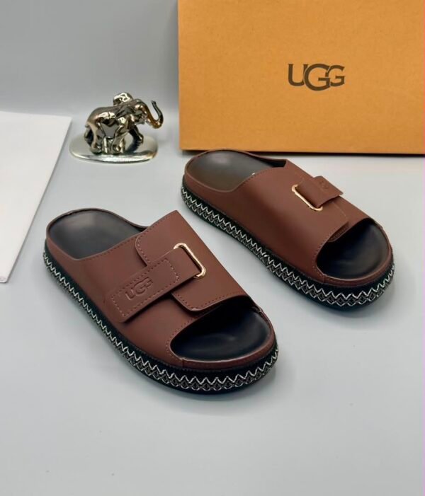 Grey UGG slide sandals with gold buckle and stitched sole, perfect for comfortable and stylish wear.