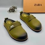 A pair of olive green strap shoes with a silver elephant figurine and Zara box in the background.