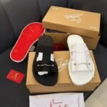 A pair of black and white Christian Louboutin sandals with red soles, boxes, and accessories on a black leather couch.