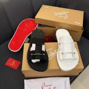 A pair of black and white Christian Louboutin sandals with red soles, boxes, and accessories on a black leather couch.