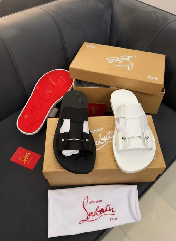 A pair of black and white Christian Louboutin sandals with red soles, boxes, and accessories on a black leather couch.