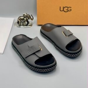 Grey UGG slide sandals with gold buckle and stitched sole, perfect for comfortable and stylish wear.