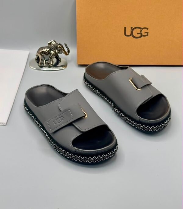 Grey UGG slide sandals with gold buckle and stitched sole, perfect for comfortable and stylish wear.