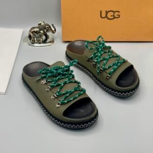 A pair of black leather UGG sandals with silver laces and stitching, displayed with a UGG box and a decorative elephant figurine.