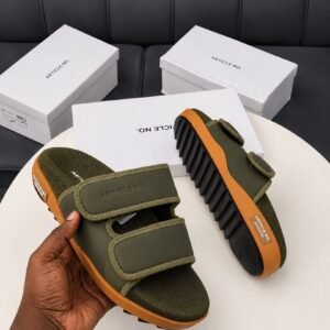 A pair of grey and orange sandals with two velcro straps, displayed on a white table with three white shoe boxes in the background.
