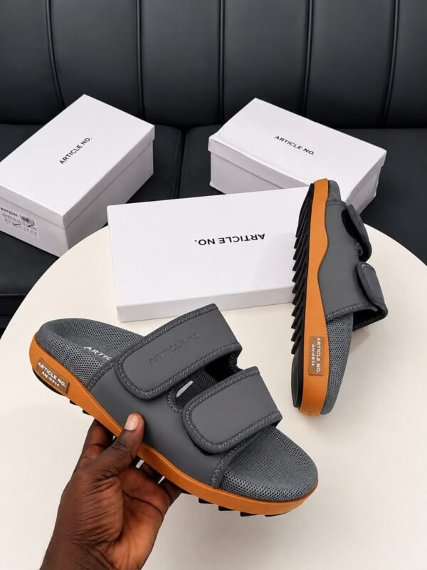 root A pair of grey and orange sandals with two velcro straps, displayed on a white table with three white shoe boxes in the background.