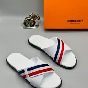 A pair of white slides with red and blue stripes, next to an orange Burberry box and a small elephant statue.