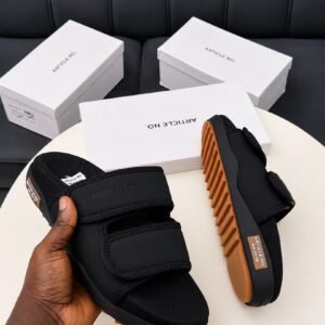 A pair of grey and orange sandals with two velcro straps, displayed on a white table with three white shoe boxes in the background.